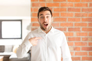 Yakışıklı işadamı ağzı açık, şaşkın ve şaşkın bir şekilde kendini işaret ediyor.