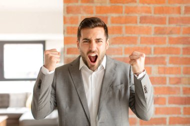Yakışıklı iş adamı öfkeli bir ifadeyle ya da yumruklarıyla başarıyı kutlarken agresif bir şekilde bağırıyor.