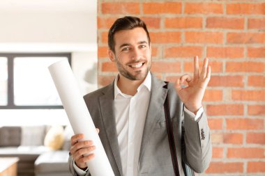 Yakışıklı mimar kendini mutlu, rahat ve tatmin olmuş hissediyor. Onayını iyi bir hareketle gösteriyor. Gülümsüyor.