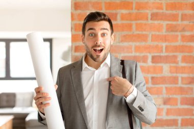 Yakışıklı mimar mutlu, şaşkın ve gururlu hissediyor, heyecanlı ve şaşkın bakışlarla kendini işaret ediyor.