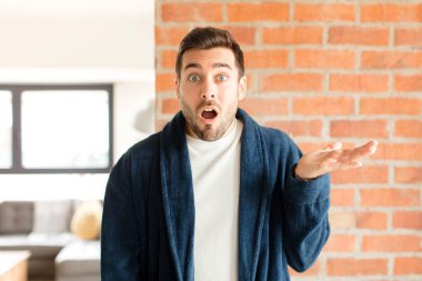 Yakışıklı adam şaşırmış ve şoka uğramış görünüyor, çenesi düşmüş, bir objeyi elinde açık bir elle tutuyor.