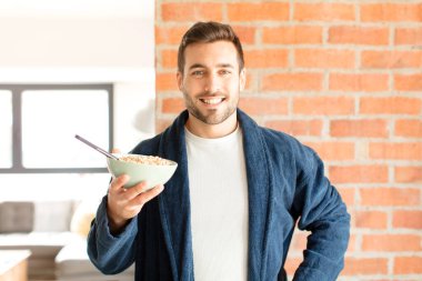 Yakışıklı adam mutlu bir şekilde gülümsüyor, eli kalçasında ve kendinden emin, olumlu, gururlu ve arkadaş canlısı.