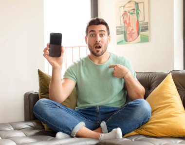 Yakışıklı adam şaşkın ve şaşkın görünüyor, ağzı açık, kendini işaret ediyor.