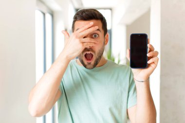 Yakışıklı adam şok olmuş, korkmuş ya da korkmuş görünüyor. Yüzü elle kaplanmış ve parmaklarının arasından gizlice bakıyor.