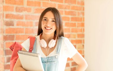 Mutlu bir şekilde gülümsüyor, eli kalçasında ve kendinden emin, olumlu, gururlu ve arkadaş canlısı bir tavırla.