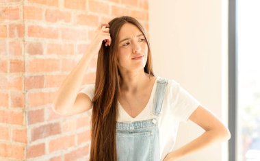 Güzel kadın şaşkın ve kafası karışmış hissediyor, başını kaşıyor ve yan tarafa bakıyor.