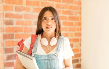 Şaşırmış ve kafası karışmış görünüyor, sinirsel bir hareketle dudağını ısırıyor, sorunun cevabını bilmiyor.