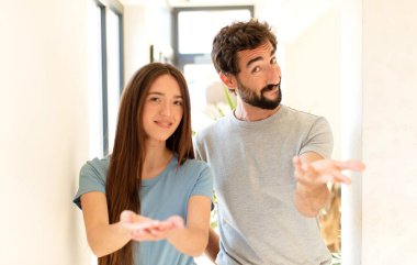 Genç çift mutlu bir şekilde gülümsüyor, kendine güveniyor, olumlu bakıyor, bir nesne ya da konsept sunuyor ve gösteriyor.