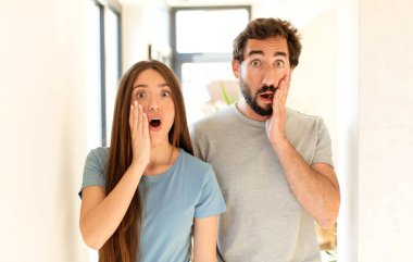 Genç çift şok olmuş ve korkmuş hissediyor, ağzı açık ve elleri yanaklarında korkmuş görünüyorlar.