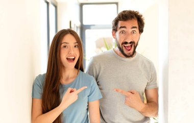 Genç çift heyecanlı ve şaşırmış görünüyor. Yana ve yukarı doğru uzayı gösteriyor.