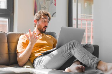 Genç sakallı adam şok olmuş, şaşırmış, endişeli ve paniklemiş hissediyor. Dizüstü bilgisayarında dizüstü bilgisayarla gergin ve dehşete düşmüş bir şekilde bakıyor.