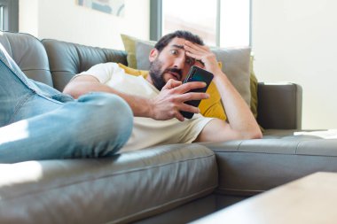 Genç sakallı adam akıllı telefonuyla kanepede dinleniyor.
