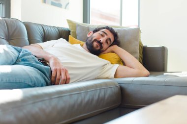 Genç sakallı adam kanepede dinleniyor.