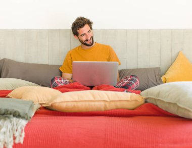 Yatakta dizüstü bilgisayarlı genç sakallı bir adam.