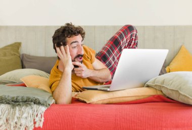 Yatakta dizüstü bilgisayarlı genç sakallı bir adam.