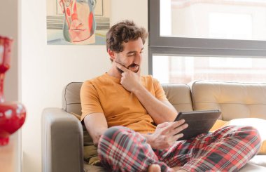 Kanepedeki sakallı genç adam Dokunmatik ekranlı tabletle