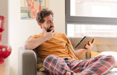 Kanepedeki sakallı genç adam Dokunmatik ekranlı tabletle