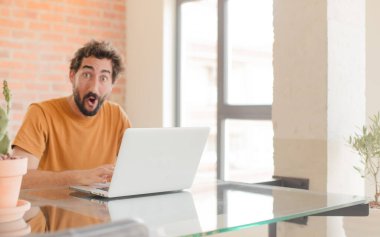 Evde dizüstü bilgisayarla çalışan sakallı genç bir adam.