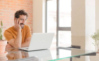 Evde dizüstü bilgisayarla çalışan sakallı genç bir adam.