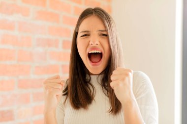 Genç bir kadın sinirli, sinirli, kızgın bakışlar ve sıkı yumruklarla bağırıyor, öfkeli hissediyor.