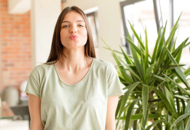 Güzel bir kadın dudaklarını birbirine bastırıyor, tatlı, eğlenceli, mutlu, sevimli bir yüz ifadesiyle, öpücük yolluyor.