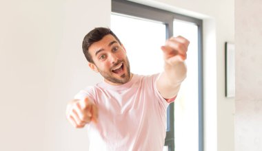 Yakışıklı adam mutlu ve kendinden emin, kamerayı iki eliyle gösteriyor ve gülüyor, seni seçiyor.