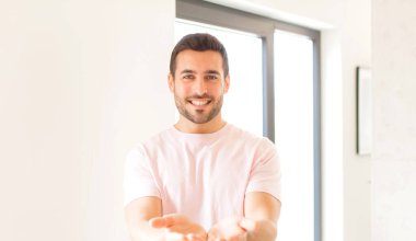 Yakışıklı adam mutlu bir şekilde gülümsüyor arkadaş canlısı, kendinden emin, olumlu bakışlı, bir nesne ya da konsept sunuyor ve gösteriyor.