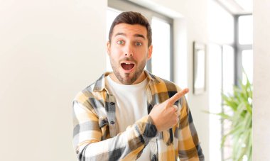 Yakışıklı adam heyecanlı ve şaşırmış görünüyor. Yana ve yukarı doğru uzayı gösteriyor.