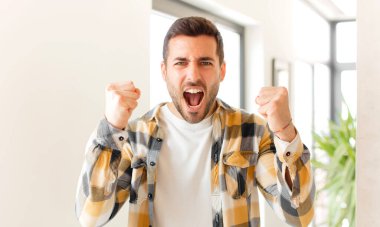 Yakışıklı adam mutlu, şaşırmış ve gururlu, bağırıyor ve başarıyı büyük bir gülümsemeyle kutluyor.