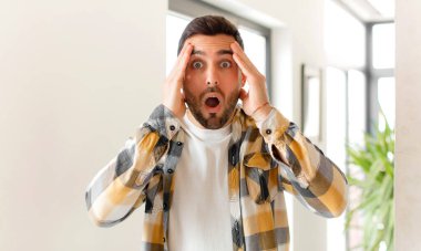 Yakışıklı adam hoş olmayan bir şekilde şaşırmış, korkmuş ya da endişeli, ağzı sonuna kadar açık ve iki kulağını da eliyle kapatıyor.