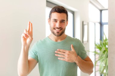 Yakışıklı adam mutlu, kendinden emin ve güvenilir görünüyor, gülümsüyor ve zafer işareti gösteriyor, olumlu bir tavırla.
