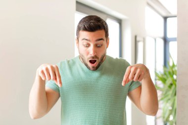 Yakışıklı adam şok olmuş, ağzı açık ve şaşkın, inançsızlık ve şaşkınlık içinde bakıyor ve onu işaret ediyor.