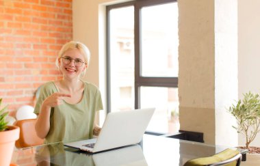 Güzel öğrenci neşeli bir şekilde gülümsüyor, mutlu hissediyor ve kenarı ve yukarıyı işaret ediyor, kopyalama alanında nesneleri gösteriyor.