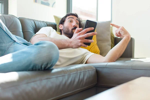 Junger Bärtiger Mann Ruht Mit Seinem Smartphone Auf Einer Couch — Stockfoto