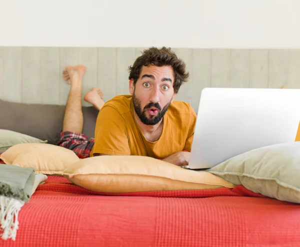 ベッドの上にノートパソコンを持った若い髭の男が — ストック写真