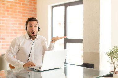 Yakışıklı tele-pazarlamacı şaşırmış ve şok olmuş görünüyor, çenesi düşmüş, bir objeyi elinde açık bir elle tutuyor.