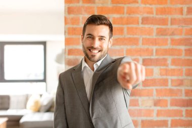 Yakışıklı iş adamı kameraya bakıyor. Tatmin olmuş, kendine güvenen, dost canlısı bir gülümsemeyle seni seçiyor.