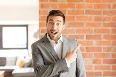 Yakışıklı iş adamı heyecanlı ve şaşırmış görünüyor. Yana ve yukarı doğru uzayı gösteriyor.
