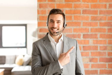 Yakışıklı pazarlamacı neşeli bir şekilde gülümsüyor, mutlu hissediyor ve yan ve yukarı doğru işaret ediyor, fotokopi uzayında nesne gösteriyor