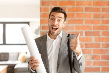 Yakışıklı mimar gururlu, kaygısız, kendinden emin ve mutlu, başparmağıyla olumlu gülümsüyor.