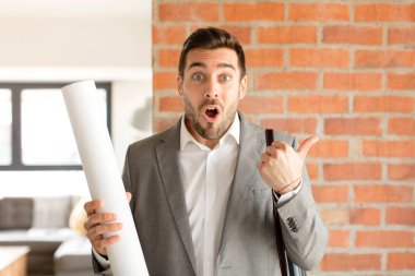 Yakışıklı mimar inançsızlıktan şaşkın şaşkın bakıyor, yan taraftaki objeyi işaret ediyor ve diyor ki: