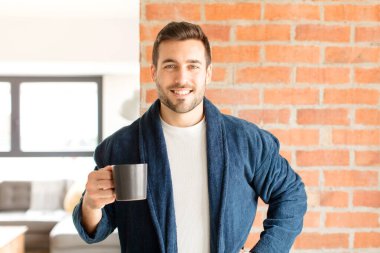 Yakışıklı adam mutlu bir şekilde gülümsüyor, eli kalçasında ve kendinden emin, olumlu, gururlu ve arkadaş canlısı.