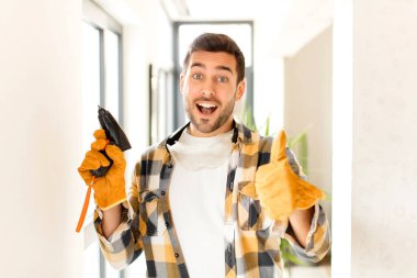 Becerikli, gururlu, tasasız, kendinden emin ve mutlu hisseden, başparmağıyla olumlu gülümseyen