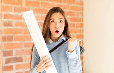 Güzel mimar inançsızlıktan şaşkın şaşkın bakıyor, yan taraftaki objeyi işaret ediyor ve diyor ki: