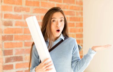 Güzel mimar şaşırmış ve şoka uğramış görünüyor, çenesi düşmüş, bir objeyi elinde açık bir elle tutuyor.