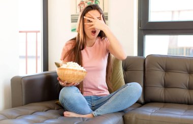 Şok olmuş, korkmuş ya da korkmuş görünüyor, yüzleri elle kaplıyor ve parmaklarının arasına bakıyor.