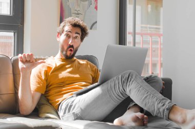 Genç sakallı adam inançsızlıktan şaşkın şaşkın bakıyor, yan taraftaki objeyi işaret ediyor ve 