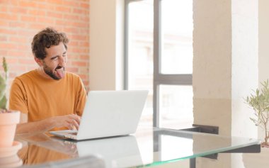 Genç sakallı, neşeli, kaygısız, asi tavırlı, şakacı ve dilsiz, eğlenen ve dizüstü bilgisayarla çalışan bir adam.