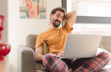 Kanepede dizüstü bilgisayarlı genç sakallı bir adam.