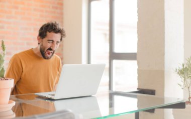 Evde dizüstü bilgisayarla çalışan sakallı genç bir adam.